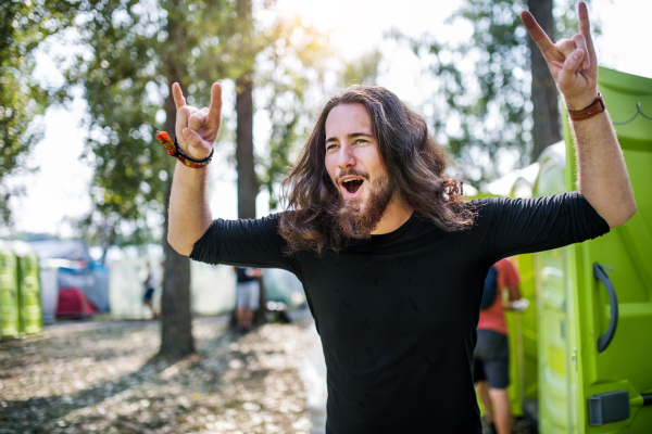 Front view of young man with long hair standing at summer festival, having fun.