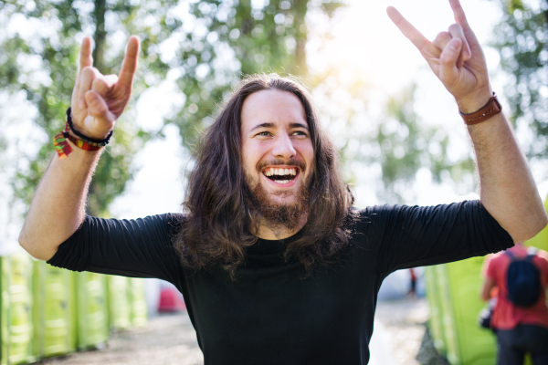 Front view of young man with long hair standing at summer festival, having fun.