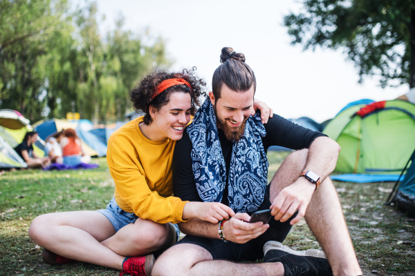 A young couple with smartphone at summer festival, sitting on the ground.