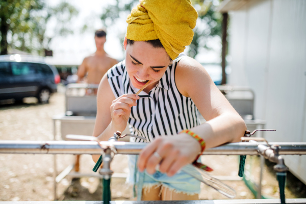 Front view of young woman at summer festival, brushing teeth by basins.