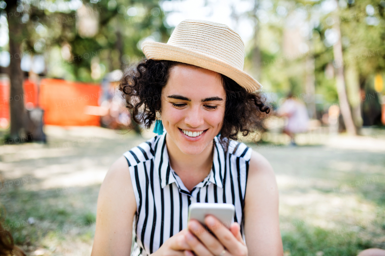 Front view of young woman at summer festival or camping holiday, using smartphone.