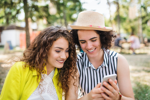 A portrait of two young women friends at summer festival, using smartphone.