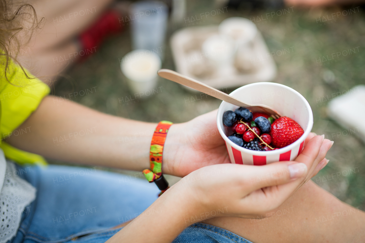 Midsection of unrecognizable woman at summer festival, sitting on the ground and eating fruit.