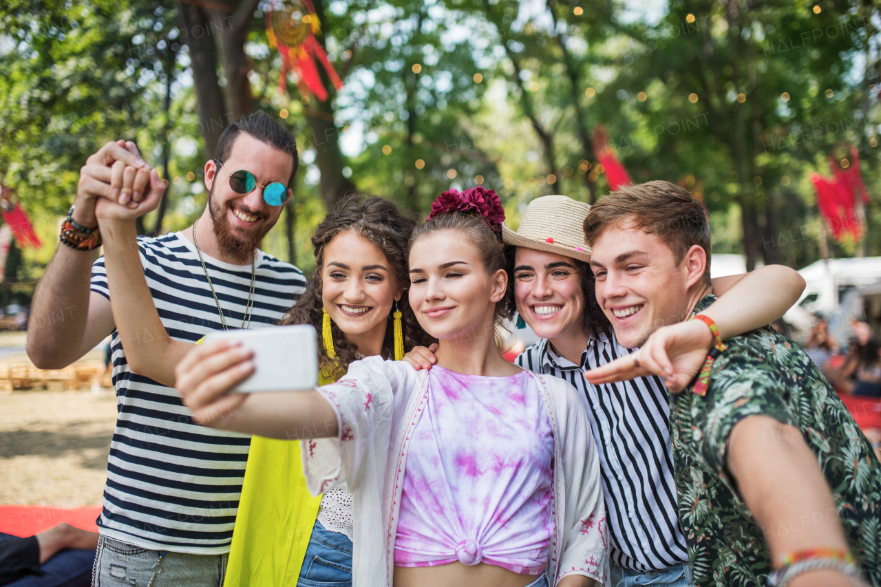 A group of young people at summer festival, taking selfie with smartphone.