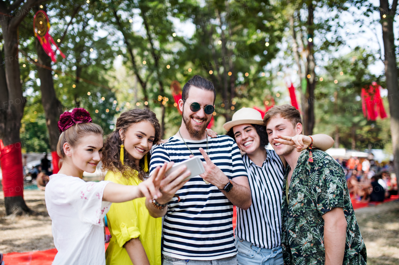 Front view of group of young friends with smartphone at summer festival, taking selfie.