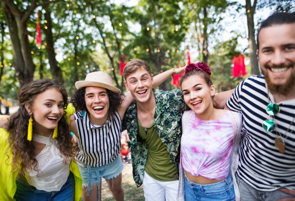 Group of young friends with smartphone at summer festival, looking at camera.