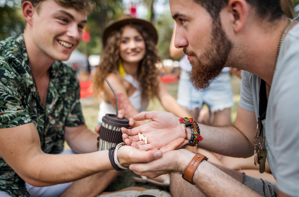 Group of young friends sitting on ground at summer festival, drug dealing concept.