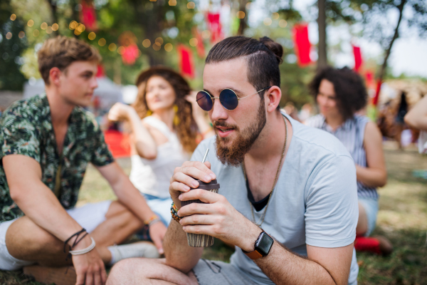 Front view of young man with sunglasses at summer festival, sitting.