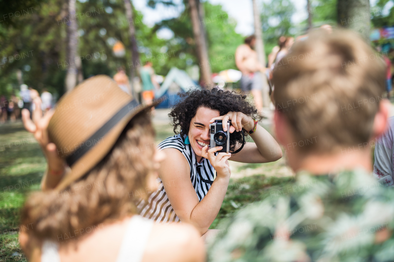 Group of young friends sitting on ground at summer festival, taking photo with camera.