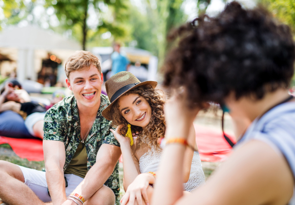 Group of cheerful young friends sitting on ground at summer festival, talking.