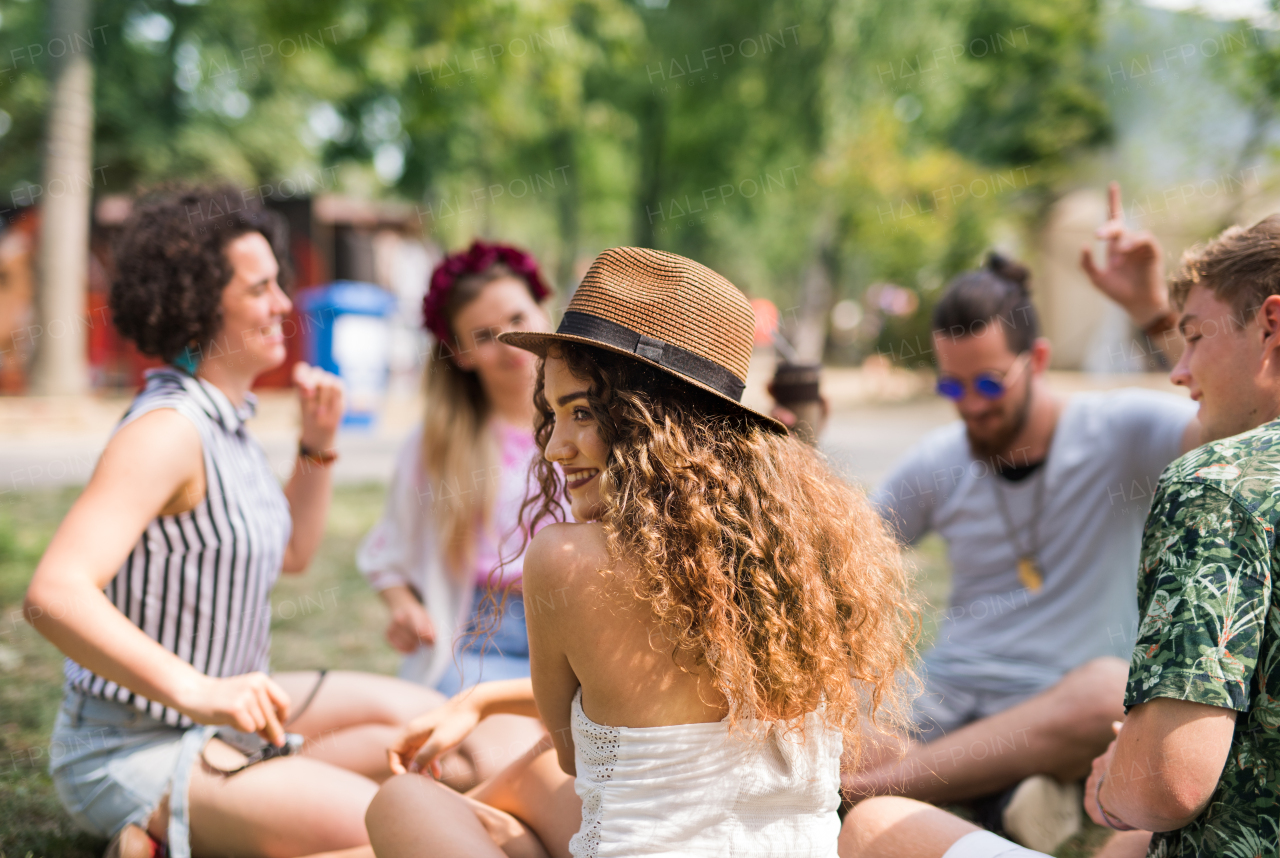 Group of cheerful young friends sitting on ground at summer festival, talking.