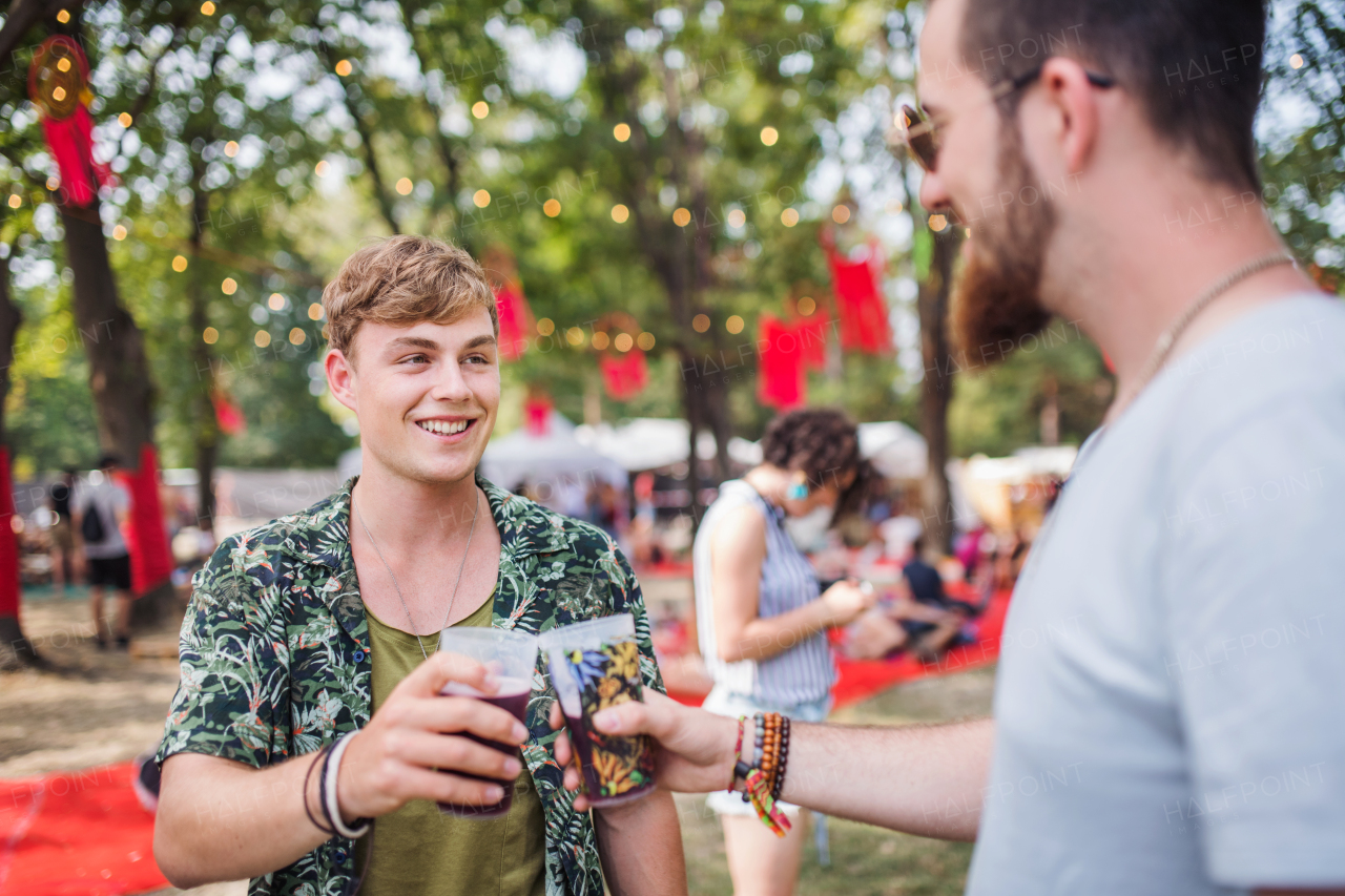 Young friends with drinks at a summer festival, clinking glasses.