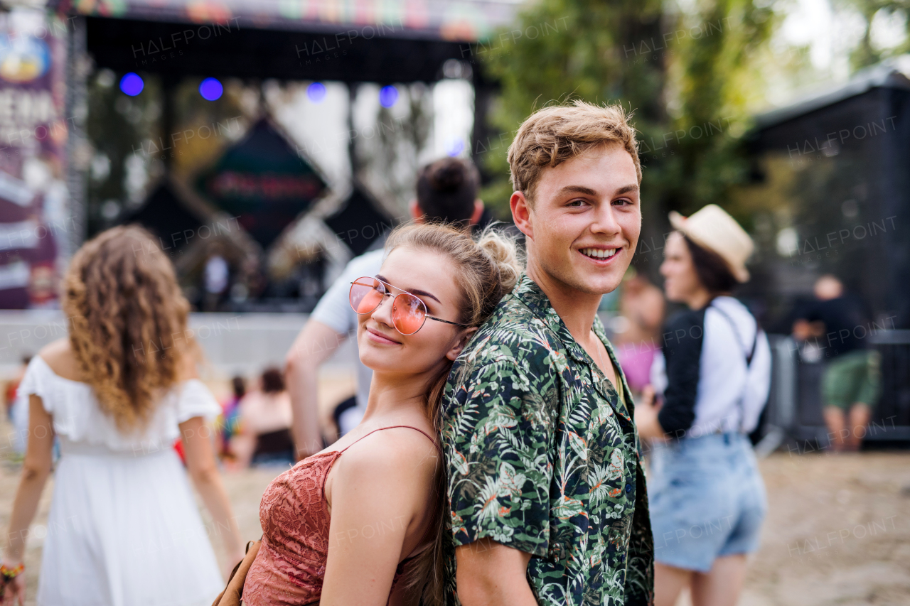 Happy young couple at summer festival, standing back to back.