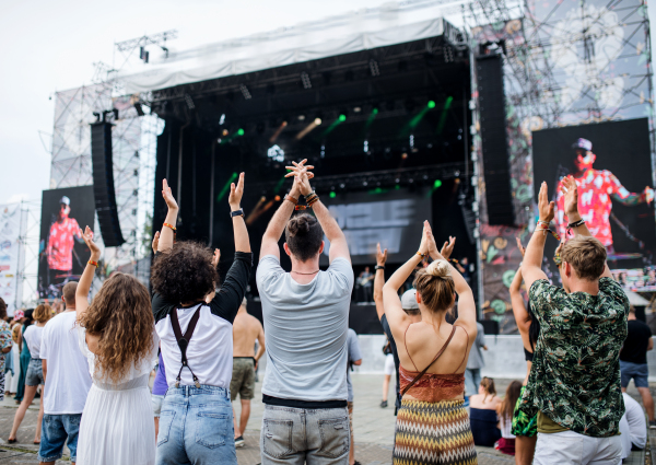 Rear view of group of unrecognizable young friends dancing at summer festival.