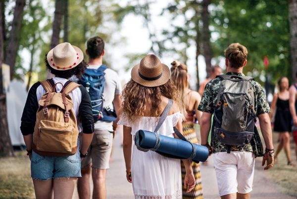 Rear view of group of young friends with backpack and mat walking at summer festival.