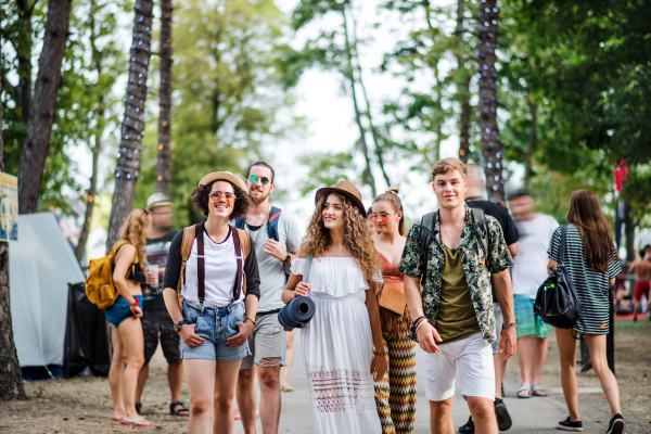 Front view of group of young friends with backpack and mat walking at summer festival.