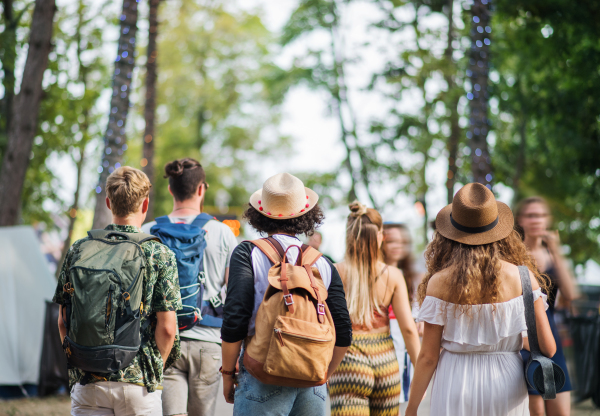 Rear view of group of young friends with backpack and mat walking at summer festival.