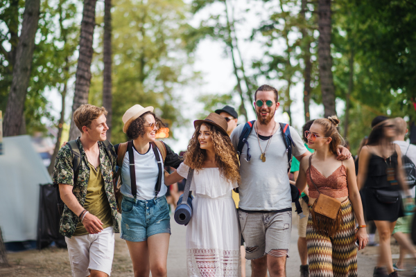 Front view of group of young friends with backpack and mat walking at summer festival.