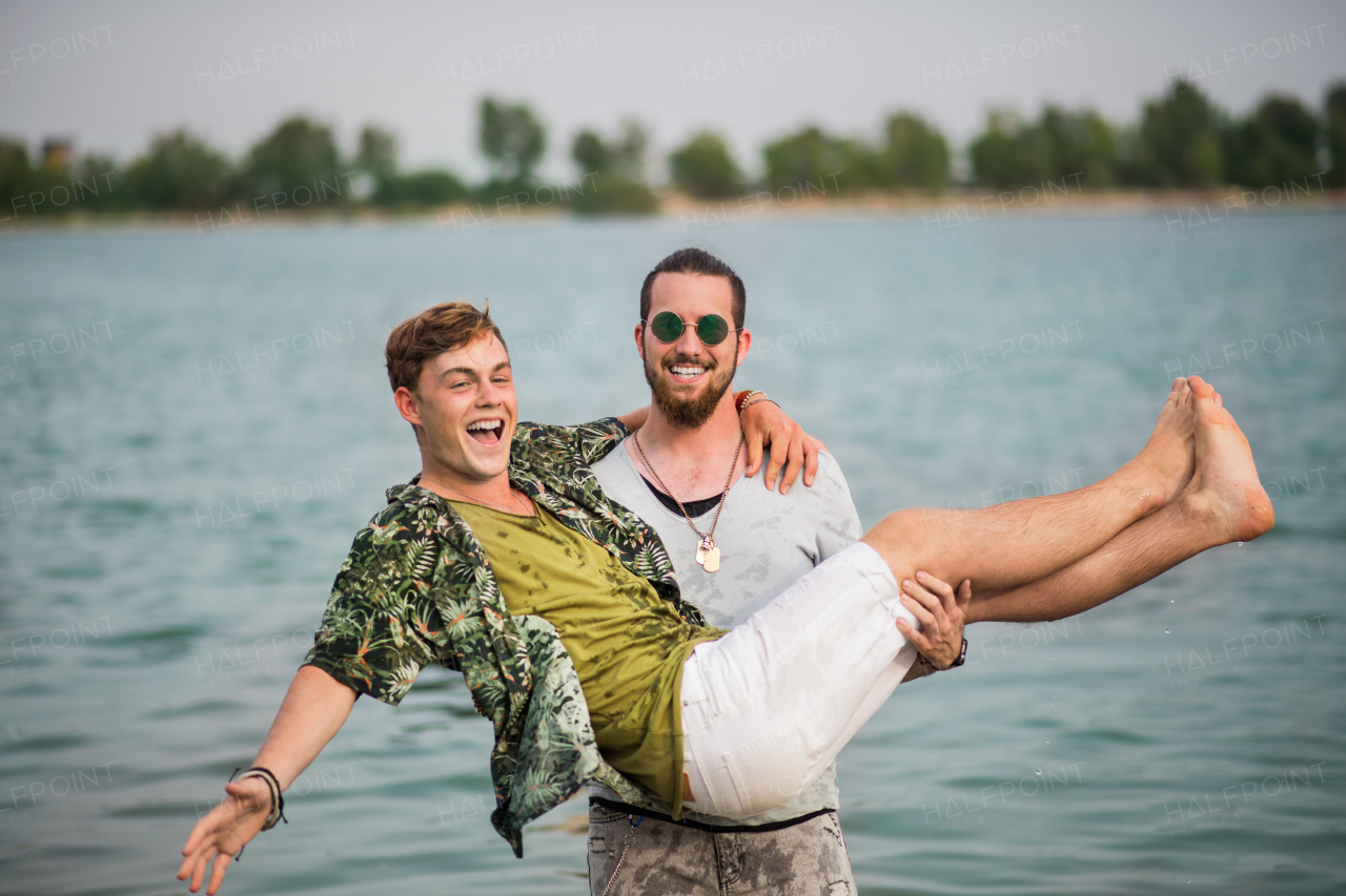 Cheerful young men friends having fun at summer festival, standing in lake.