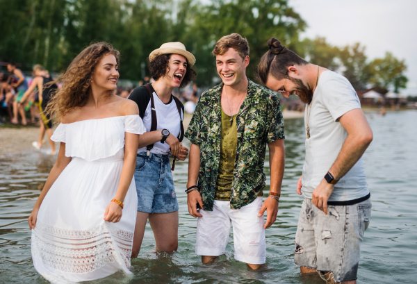 Group of young friends at summer festival, standing in water in lake.