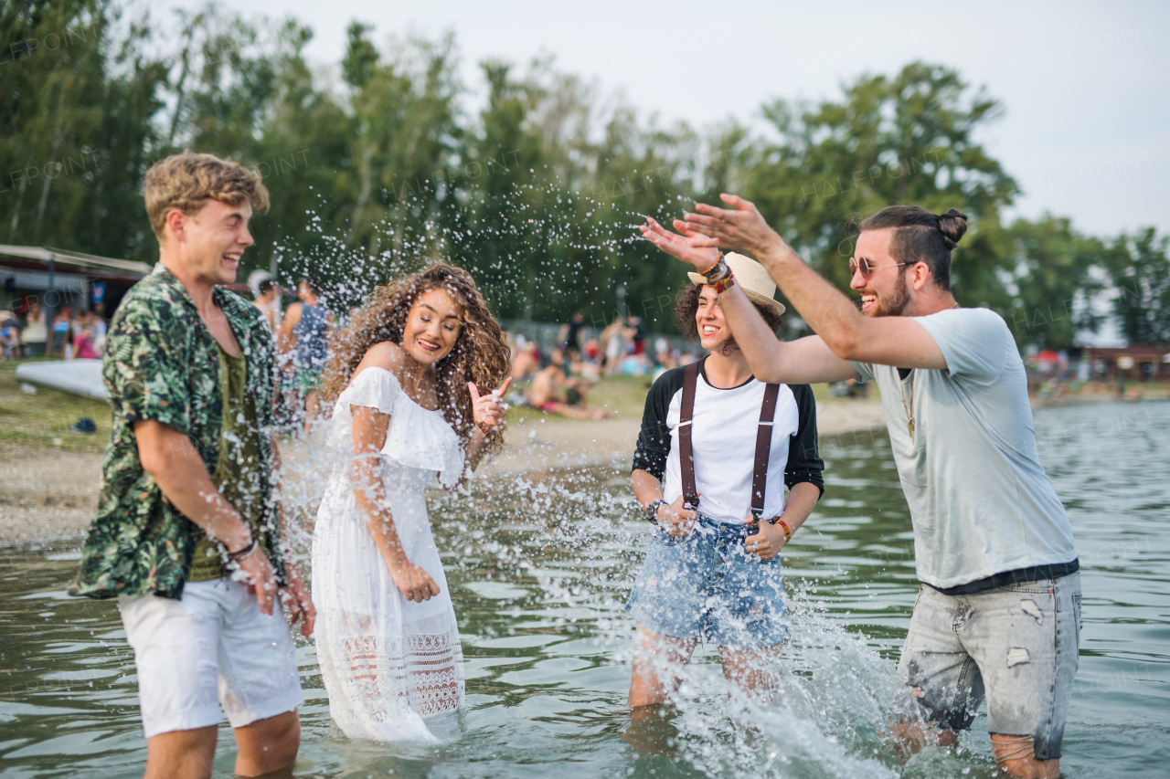 Group of young friends at summer festival, standing in lake and splashing water.