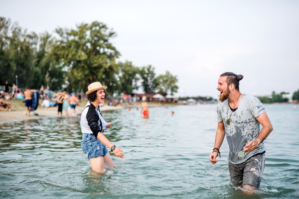 Young laughing couple standing in lake at summer festival, having fun.