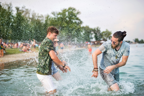 Cheerful young men friends having fun at summer festival, standing in lake.