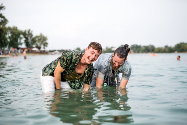 Wet young men friends at summer festival, standing in lake and looking at camera.