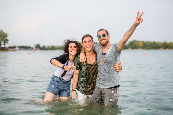 Group of young friends at summer festival, standing in water in lake.