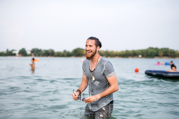 Young wet man having fun at summer festival, standing in lake. Copy space.