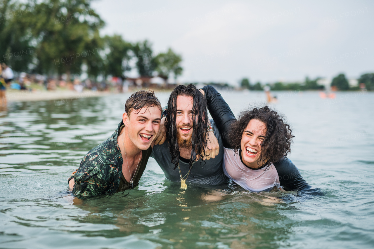 Group of wet young friends at summer festival, standing in lake and looking at camera.