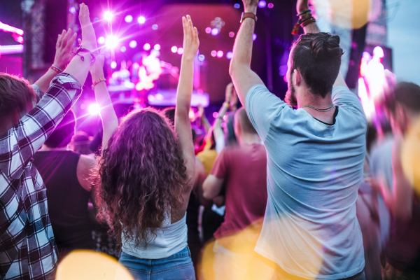 Rear view of group of unrecognizable young friends dancing at summer festival.