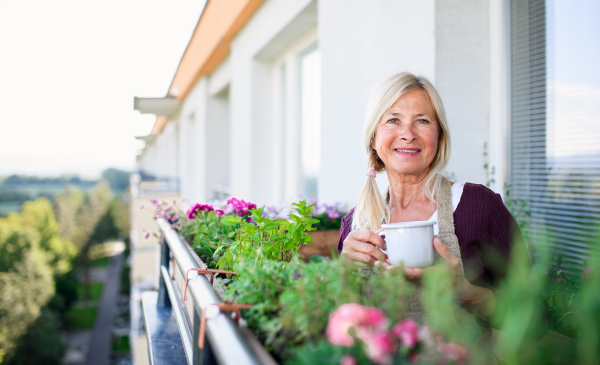 Portrait of senior woman with coffee gardening on balcony in summer, looking at camera.