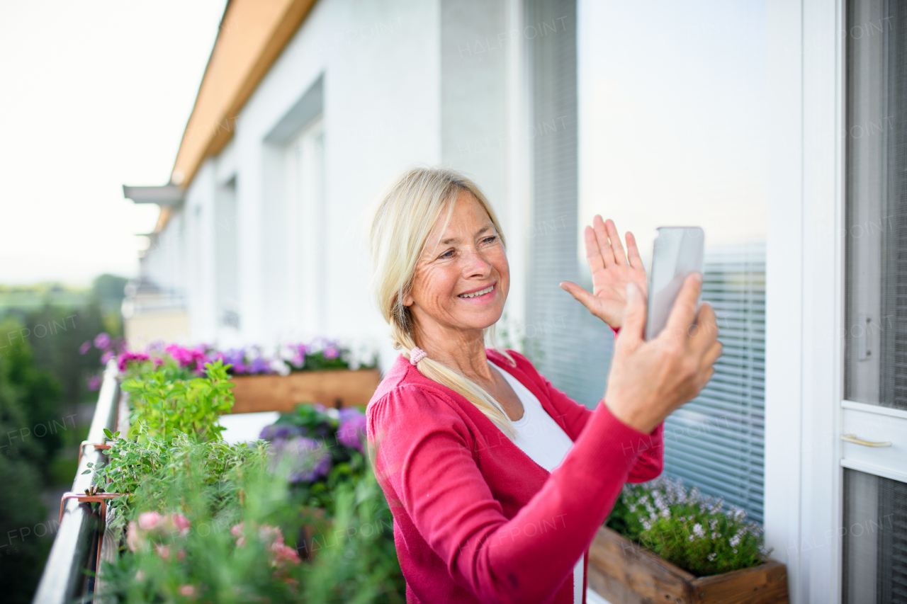 A senior woman with smartphone relaxing on balcony in summer, video call concept.