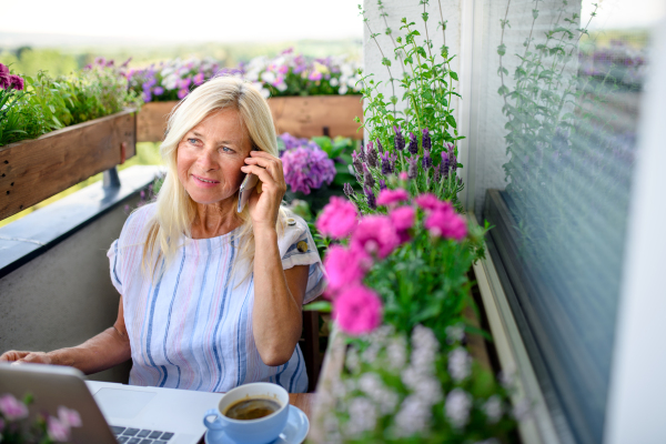 Active senior woman with laptop and smartphone working on balcony in summer, home office.