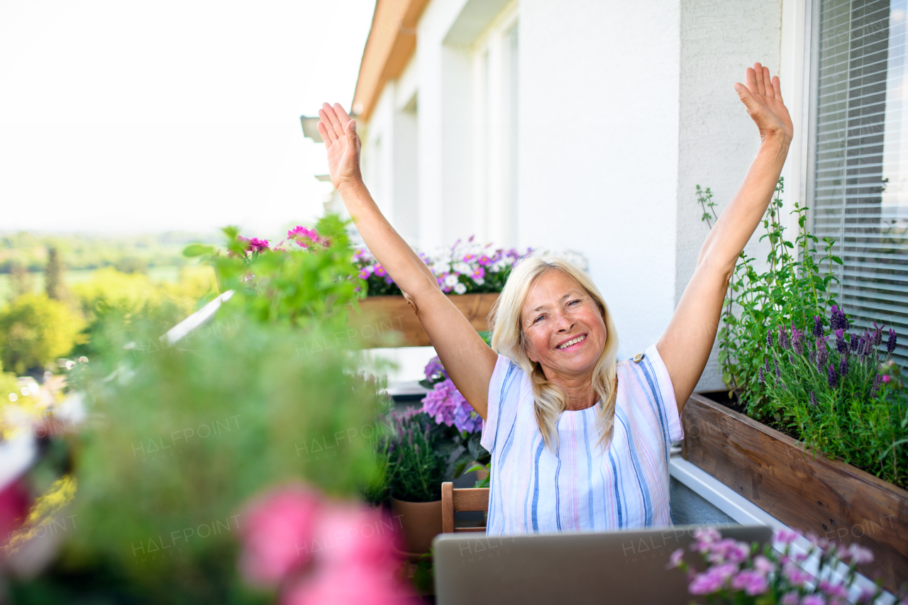 Active senior woman with laptop stretching when working on balcony, home office concept.