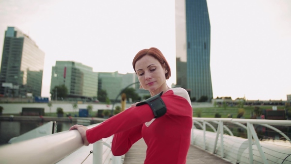 A young woman resting after doing exercise on bridge outdoors in city, using smartphone. Slow motion.