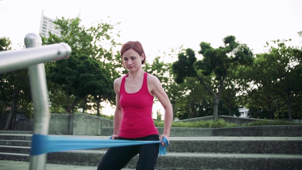 Full length portrait of young woman doing exercise outdoors in city with elastic bands. Slow motion.