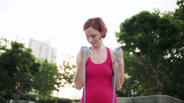 Full length portrait of young woman doing exercise outdoors in city with elastic bands. Slow motion.