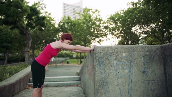 Young woman doing exercise outdoors in city, stretching. Slow motion.