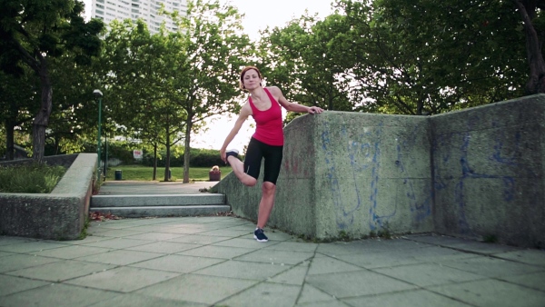 Young woman doing exercise outdoors in city, stretching. Slow motion.