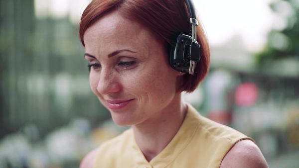 Young businesswoman with headphones sitting in cafe outdoors in city, working. Slow motion.