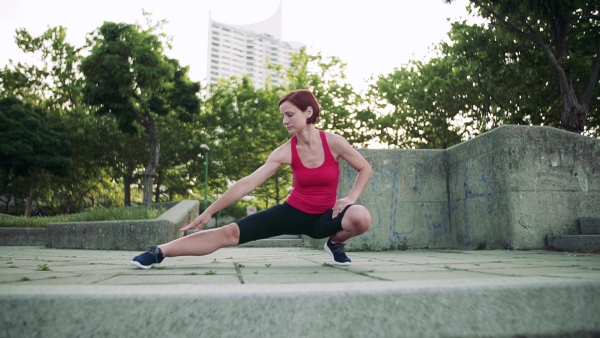 Young woman doing exercise outdoors in city, stretching. Slow motion.