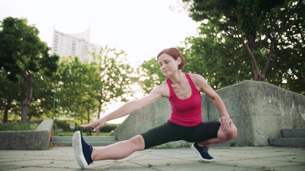 Young woman doing exercise outdoors in city, stretching. Slow motion.