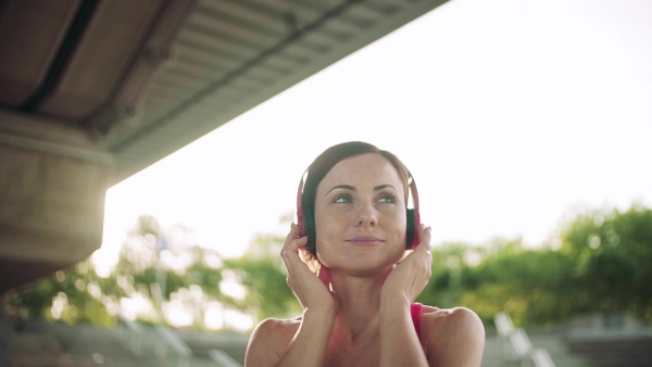 A young woman with headphones resting after doing exercise outdoors in city. Slow motion.