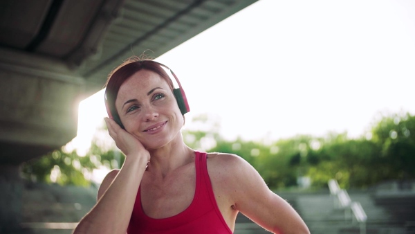 A young woman with headphones resting after doing exercise outdoors in city. Slow motion.