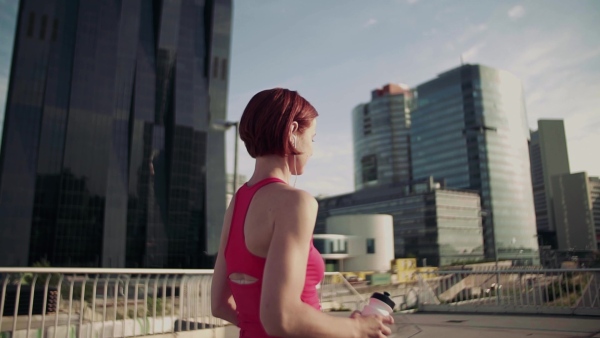 Young woman with earphones on bridge outdoors in city, resting after exercise. Slow motion.