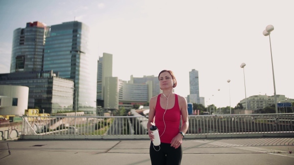 Young woman with earphones on bridge outdoors in city, resting after exercise. Slow motion.