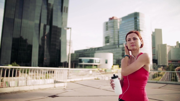 Young woman with earphones on bridge outdoors in city, resting after exercise. Slow motion.