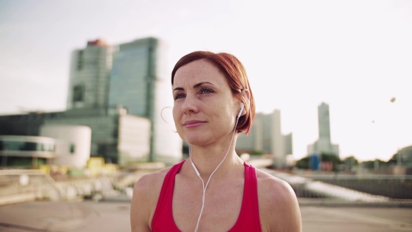 Young woman with earphones on bridge outdoors in city, resting after exercise. Slow motion.